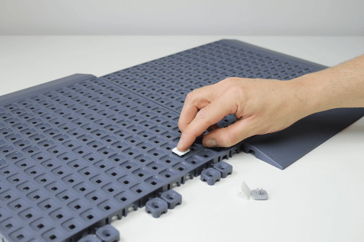 Person assembling interlocking gray plastic mats on a white surface